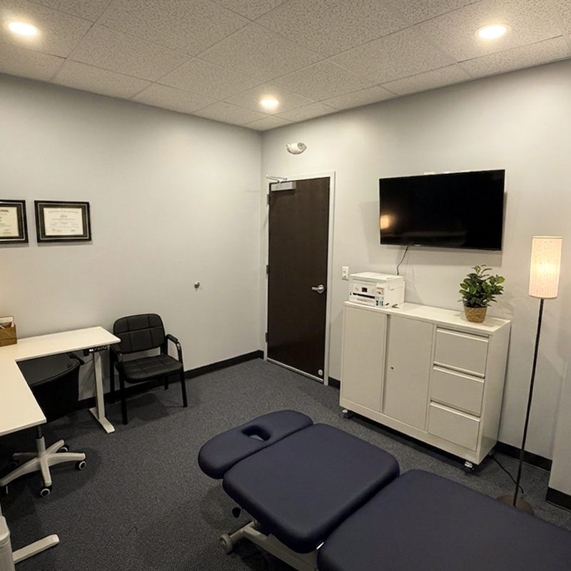 Vertigo Solutions treatment room with treatment table, desk, and framed credentials on the wall